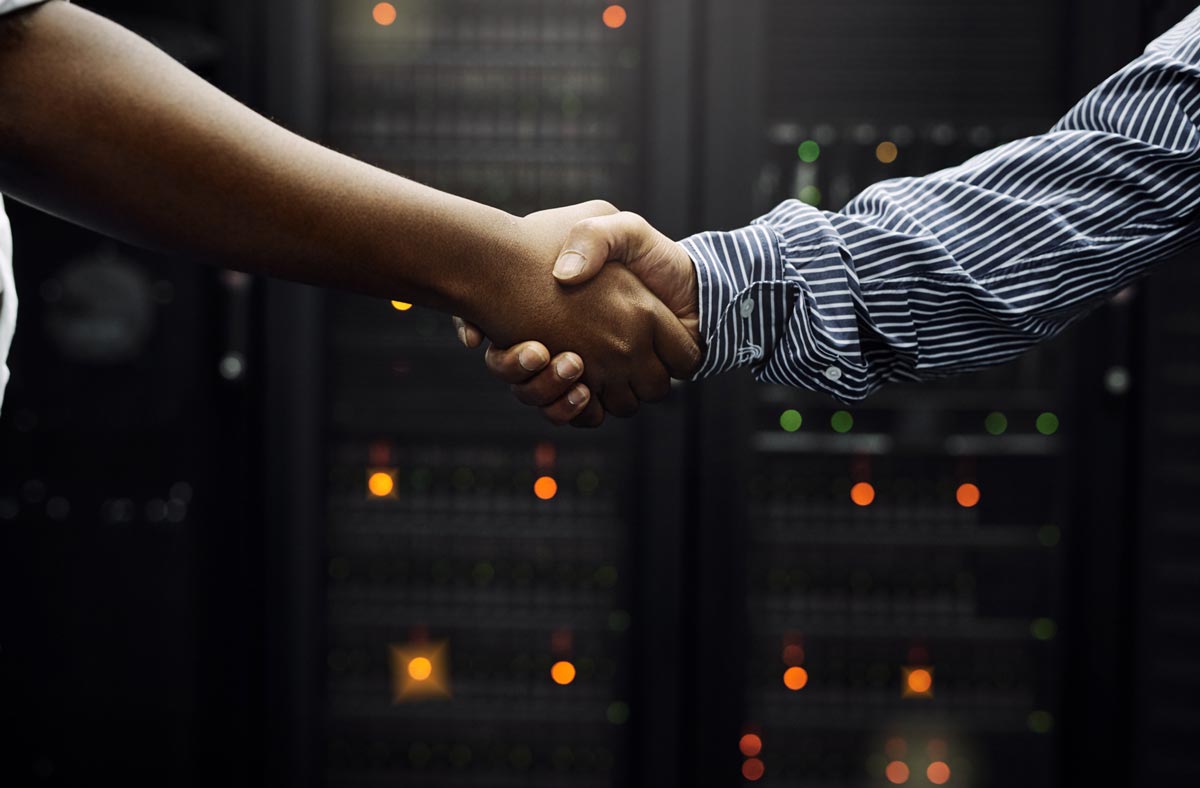 Two people shaking hands in front of a row of servers