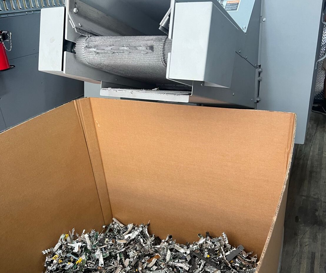 An industrial shredder dispensing shredded hard-drive scrap into a cardboard box